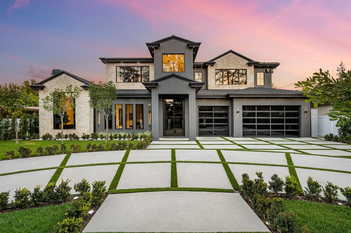 Modern home with a large driveway and a beautifully landscaped front yard at sunset